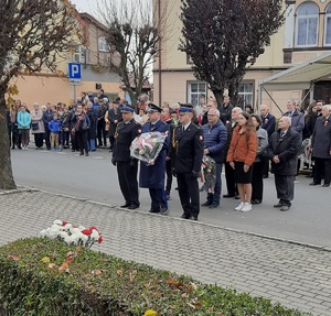 przedstawiciele służb mundurowych pod pomnikiem ofiar przemocy i wojen w Krapkowicach, składają kwiaty, w tle mieszkańcy miasta