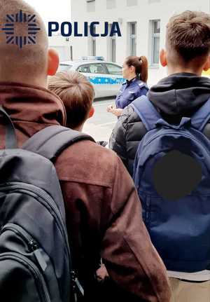 policjantka, radiowóz, trzech uczniów w tle budynek komendy powiatowej policji w Krapkowicach