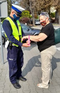 Obok ulicy, policjant zakłada kobiecie opaskę odblaskową na rękę