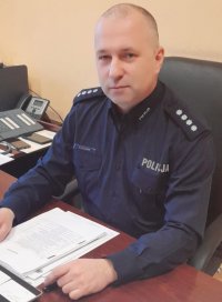 Komendant Powiatowy Policji w Krapkowicach, przy biurku, na biurku dokumenty w tle sprzęt elektroniczny