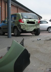 samochód osobowy hyundai z uszkodzeniami tyłu pojazdu na parkingu marketu, w tle budynek marketu, element zderzaka pojazdu na parkingu
