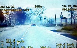 widok z ekranu wideorejstratora, samochodu nieoznakowanego policji, na ekranie widoczny liczby wskazujące prędkość oraz inne parametry,widoczny również w oddali samochód osobowy, jezdnia,zabudowania i drzewa