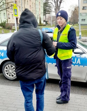 policjantka kontrolująca pieszego w rejonie przejścia dla pieszych, w tle radiowóz