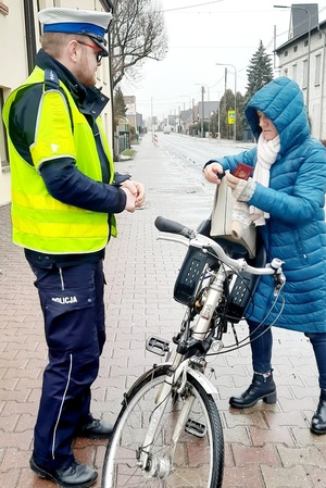 policjant kontrolujący rowerzystkę, stoją na chodniku, w tle jezdnia i widoczne przejście dla pieszych