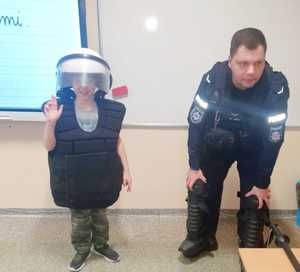 policjant i chłopiec ubrany w wyposażenia policyjne służące do ochrony ciała na zabezpieczeniach imprez masowych, hełm i kamizelkę