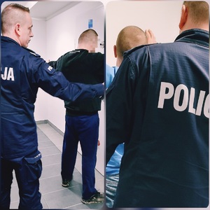 obraz przedstawia dwóch mężczyzn zatrzymanych, jeden ubrany w czarne sportowe, ubrania, drugi, widoczna tylko górna część ciała, w niebieskiej bluzie. Na zdjęciu policjant sprawdza zatrzymanych pod kątem posiadania przedmiotów niebezpiecznych