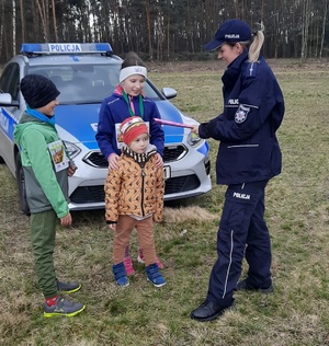 policjantka rozdająca dzieciom odblaski, w tle radiowóz