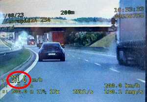 ekran videorejestratora z wskazaniami pomiarów, na ekranie w oddali samochód osobowy