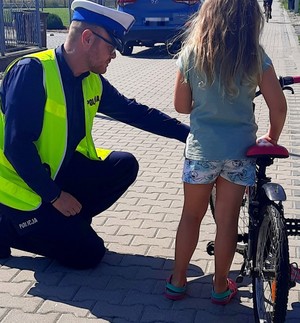 dziewczynka przy rowerze i policjant tłumaczący jej warunki jego wyposażenia