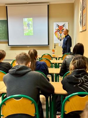 Uczniowie w sali wraz z funkcjonariuszami, którzy omawiają specyfikę służby i pracy w Policji