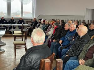 Debata społeczna. Grafika przedstawia uczestników Debaty. W tle znajdują się funkcjonariusze policji