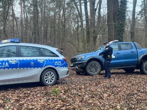 Grafika przedstawia pojazdy policji i straży leśnej. W tle znajduje się las, na terenie którego pełniona jest służba przez funkcjonariuszy obydwu służb.