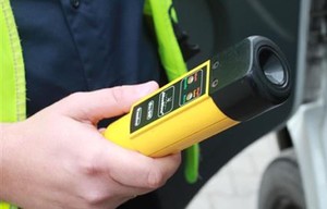 na zdjęciu znajduje się policjant, który w rękach urządzenie do pomiaru zawartości alkoholu w organizmie