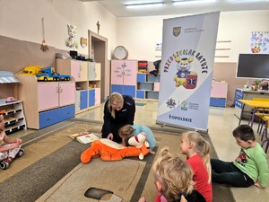 Funkcjonariuszka biorąca udział w spotkaniu &quot;Przedszkolak ratuje&quot;. Wraz z przedszkolakami uczy w jaki sposób udzielić pomocy przedmedycznej.