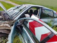 Rozbity samochód osobowy marki ford, zniszczony znak drogowy z symbolem czerwonych strzałek