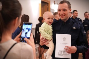 Zdjęcie przedstawia policjanta  z dzieckiem na rękach.