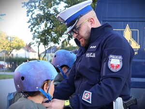 zdjęcie kolorowe: policjanci rozdają dzieciom kaski i elementy odblaskowe